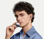 Male model wearing HUAWEI FreeClip 2 Special Edition Space Silver open-ear earbud while holding the metallic round charging case